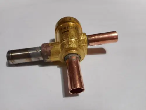 Elektroventil von Remeha mit drei Anschlüssen, zwei Kupferrohren und einem zentralen Verbindungselement. Für Anwendung in Heizungs- oder Flüssigkeitssystemen geeignet.